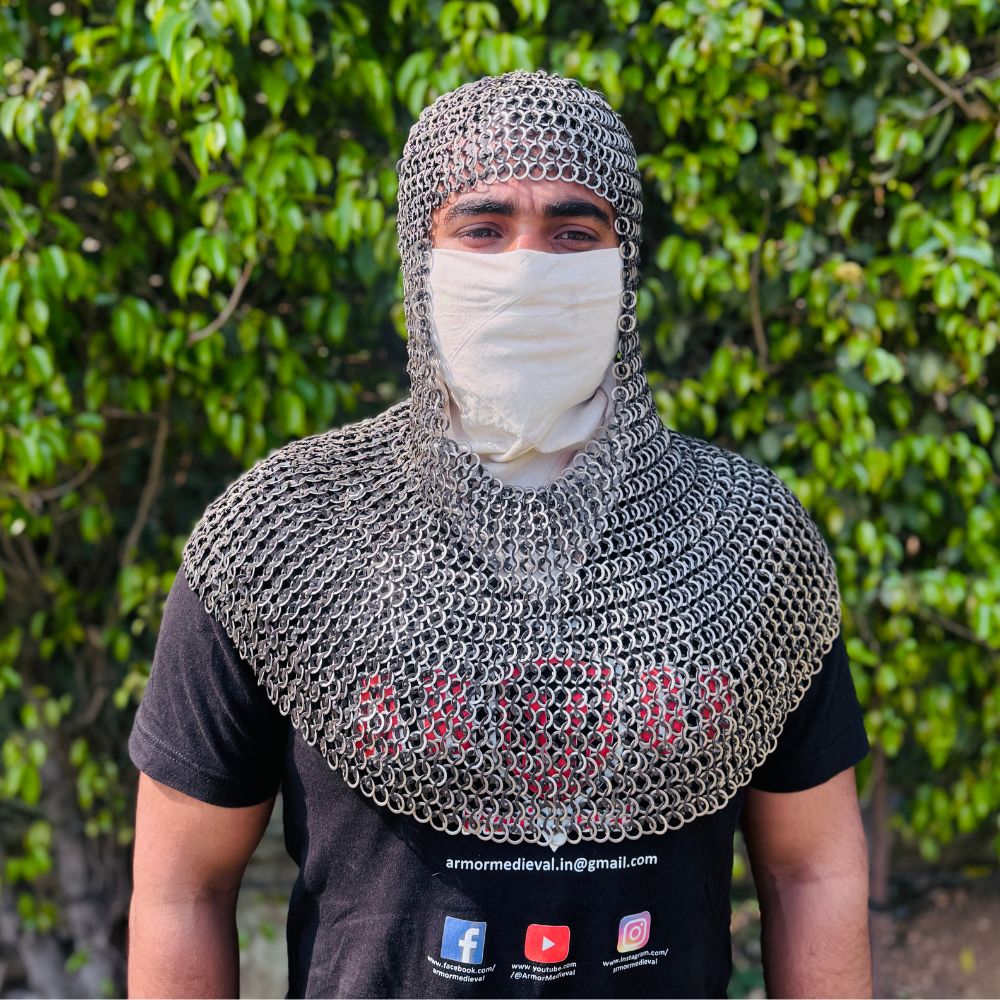 May include: A silver chainmail coif, a type of medieval head and neck protection. The coif is made of small, interlocking metal rings and covers the head, neck, and shoulders. The coif is worn over a brown garment.